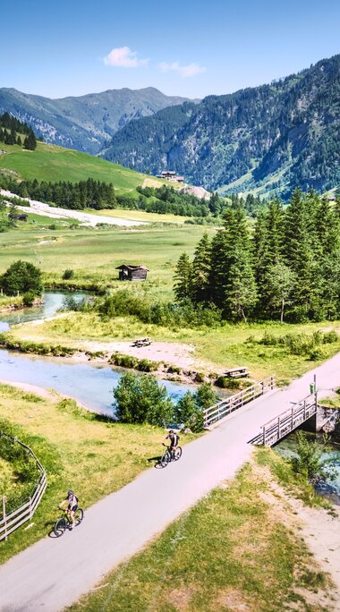 Cyclists crossing a bridge in a green valley landscape. | © Daniel KOgler
