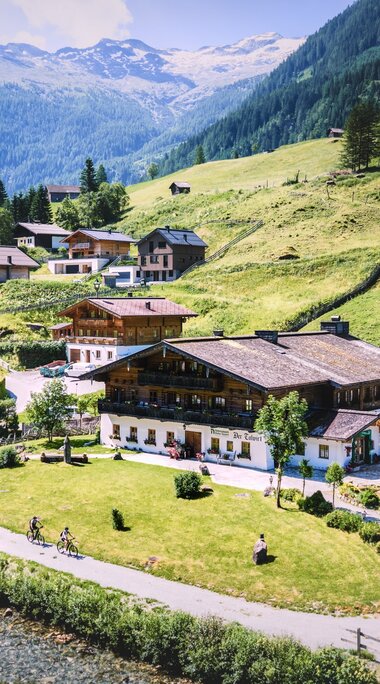 Alpenhof und Häuser in grüner Berglandschaft im Tal. | © Daniel Kogler