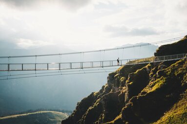 Person überquert eine Hängebrücke in den Bergen, mit Aussicht auf ein Tal. | © Ferienregion Nationalpark Hohe Tauern - Gerald Demolsky