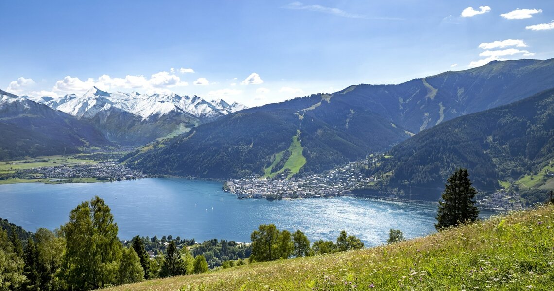 Blick auf einen See, umgeben von Bergen mit Schneegipfeln und einer blühenden Wiese im Vordergrund. | © Zell am See Kaprun Tourismus