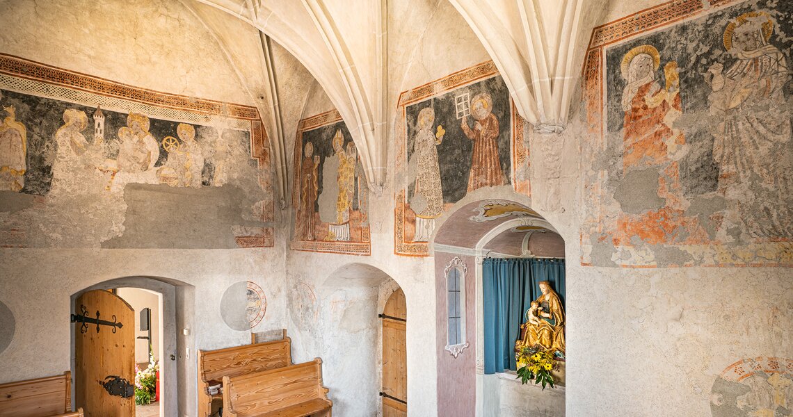 Innenansicht der Michaelskapelle mit historischen Wandmalereien und Holzbankreihen. | © Ferienregion Nationalpark Hohe Tauern