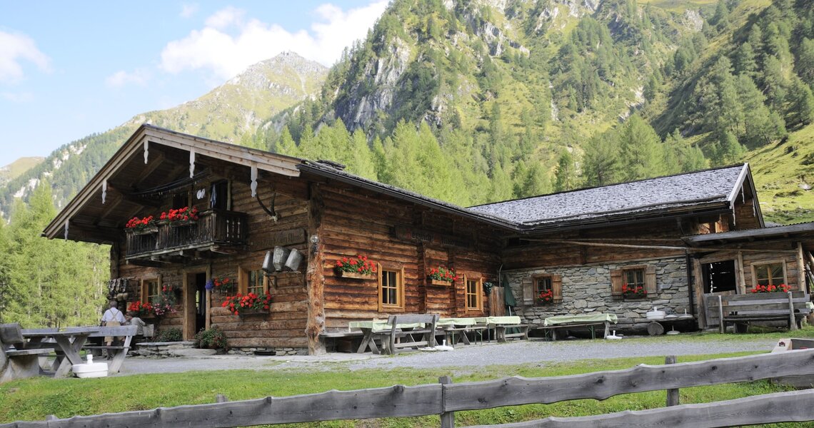 Traditionelle Almhütte mit Blumenbalkonen in idyllischer Berglandschaft. | © Ferienregion Nationalpark Hohe Tauern
