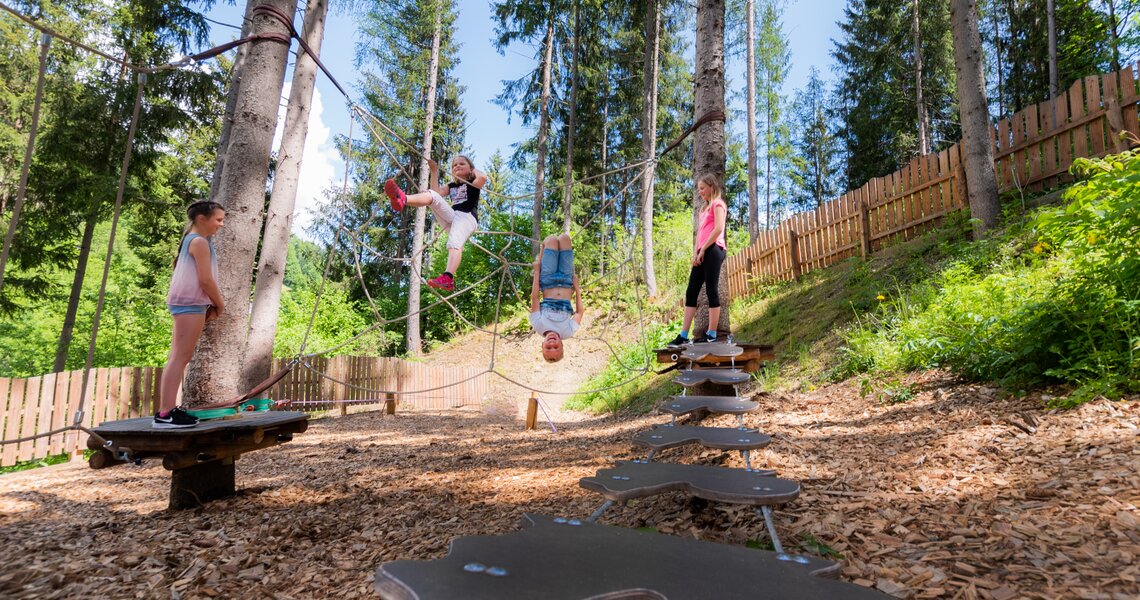 Kinder spielen im Hochseilgarten inmitten eines Waldes mit Holzspänen am Boden. | © Ferienregion Nationalpark Hohe Tauern