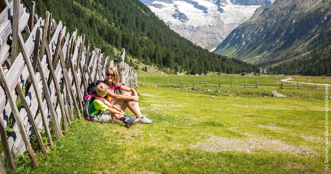 Mutter und Kind sitzen an einem Holzzaun mit Blick auf das Krimmler Achental und die Berge. | © Ferienregion Nationalpark Hohe Tauern