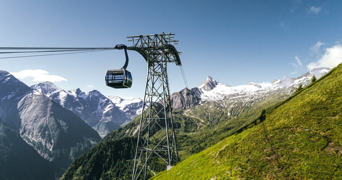 A modern cable car hovers over a green landscape with mountain peaks in the background. | © Kitzsteinhorn Talstation