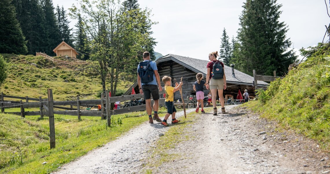 Family with children walking on a trail to a mountain hut, green meadows and forest in the background. | © Holiday Region National Park Hohe Tauern
