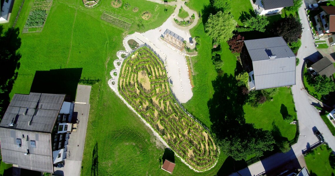 Luftaufnahme eines Gartens mit geometrischen Wegen und Grünflächen in einer Dorflandschaft. | © Ferienregion Nationalpark Hohe Tauern