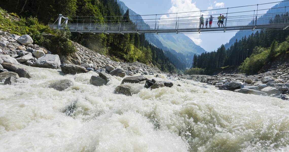 Hängebrücke über einen tosenden Gebirgsbach, eingerahmt von Bergen und Wald. | © Ferienregion Nationalpark Hohe Tauern