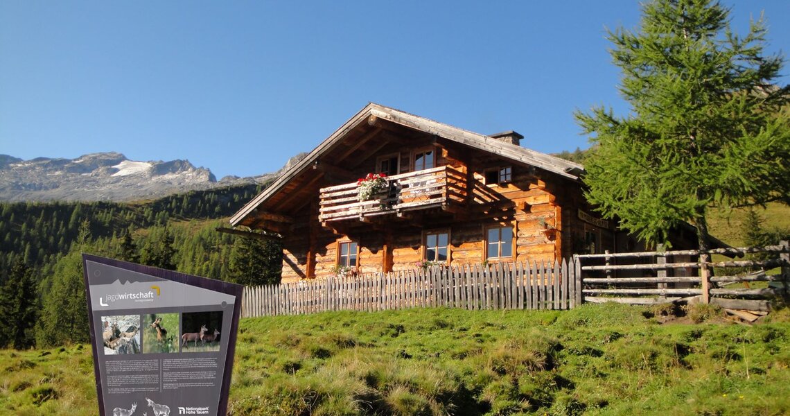 Rustikale Berghütte aus Holz mit Infotafel vor alpiner Landschaft im Nationalpark Hohe Tauern. | © Ferienregion Nationalpark Hohe Tauern