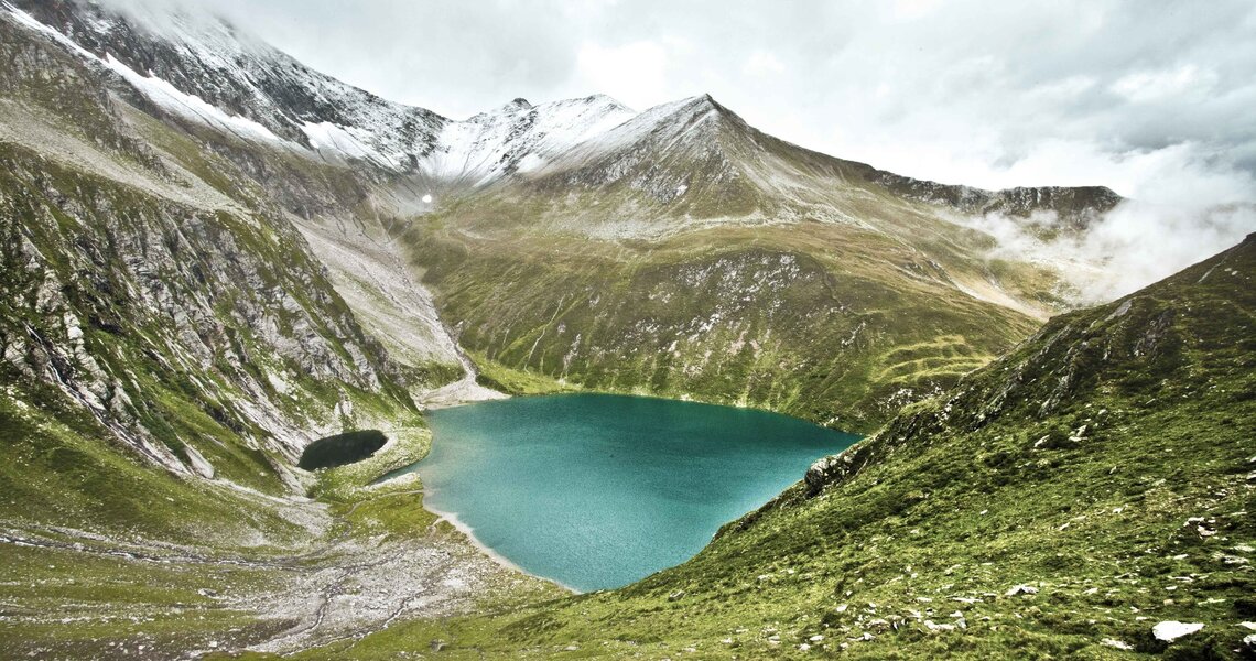 Türkisfarbener Bergsee, umgeben von steilen Berghängen und Wolken. | © Ferienregion Nationalpark Hohe Tauern