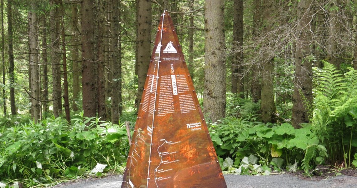 Rostfarbene Infotafel in Pyramidenform im Wald mit detaillierten Beschreibungen. | © Ferienregion Nationalpark Hohe Tauern