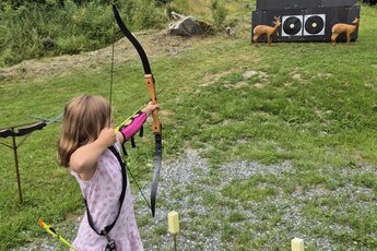Child practicing archery on a meadow with targets in the background. | © Bogensport Vorderegger
