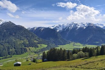 Panoramic view across a green valley towards forested mountain slopes and snow-covered peaks of the Hohe Tauern. | © Bogensport Vorderegger