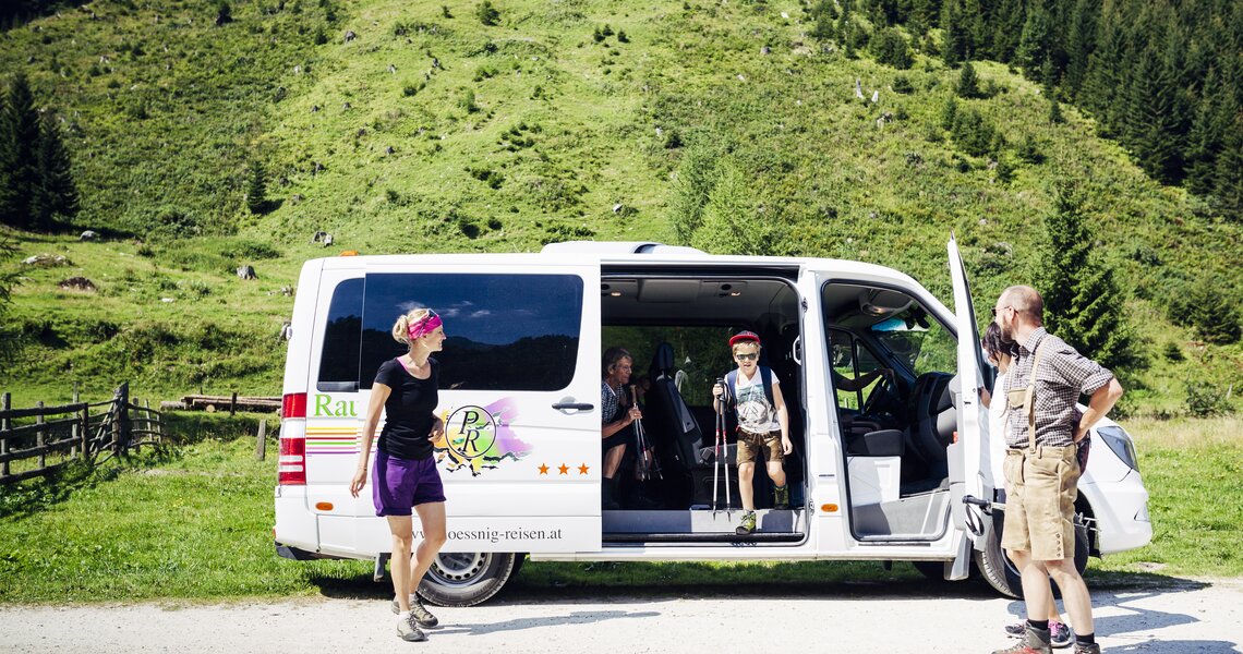 Wanderer steigen aus einem Nationalparktaxi in grüner Almlandschaft aus, umgeben von Wäldern. | © Seidlwinkl Nationalpark Taxi