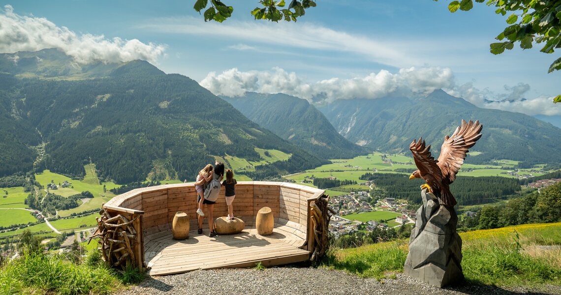 Viewing platform with family and eagle sculpture overlooking valley, mountains and village. | © © Wildkogel-Arena Neukirchen & Bramberg