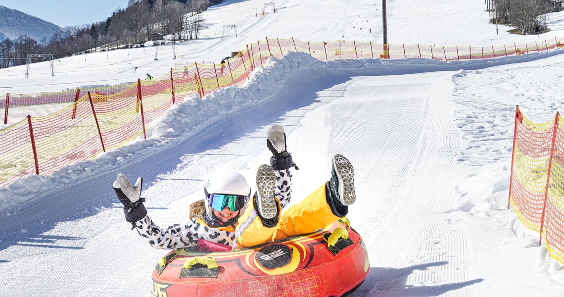Child snow tubing on a snowy slope, enjoying fun and speed. | © TVB Piesendorf Niedernsill - Harry Liebmann