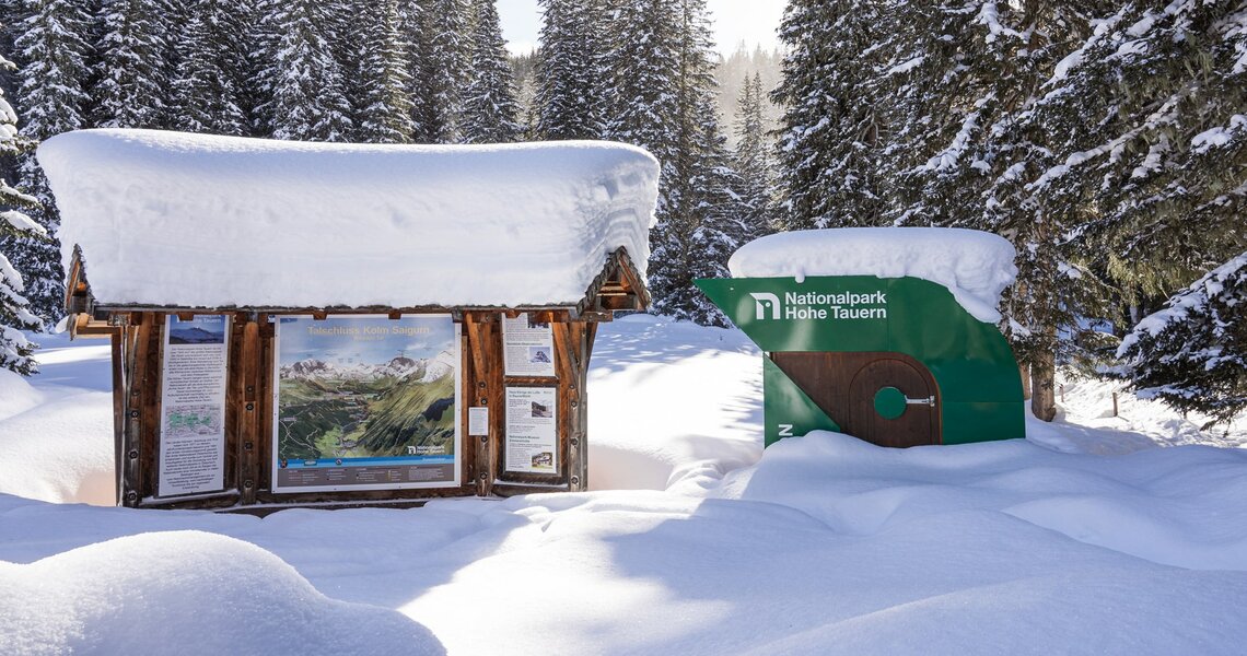 Informationstafel des Nationalparks Hohe Tauern, umgeben von verschneiten Wäldern im Winter. | © Branislav Rohal