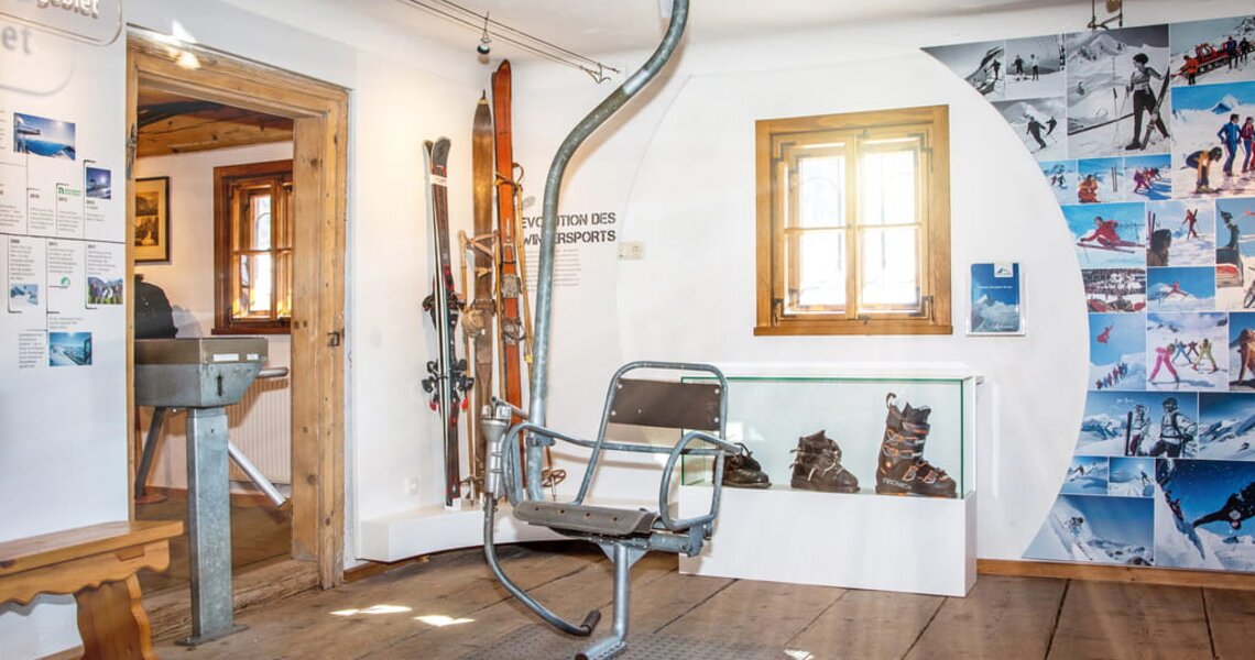 Exhibit on skiing history with historic chairlift seat, old skis and ski boots in the room. | © Optimarlies.at