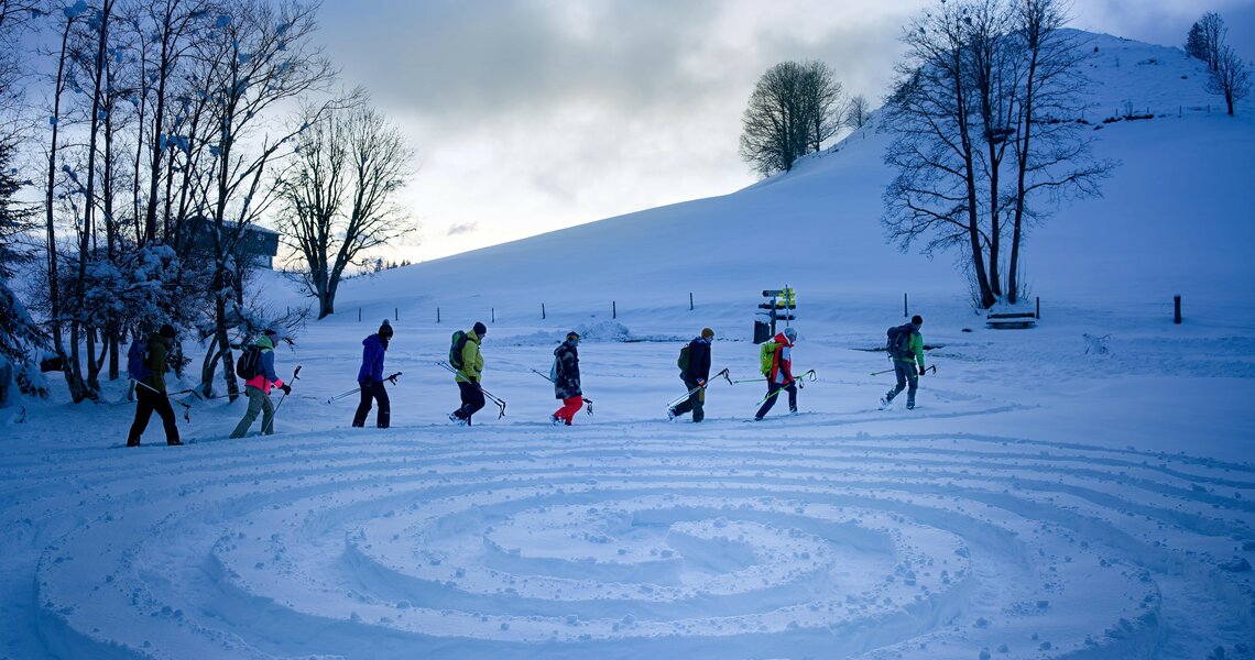 Gruppe von Schneeschuhwanderern in einer verschneiten Landschaft mit einem im Schnee gezeichneten Labyrinth. | © Florian Kreidl Glück