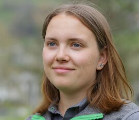 Employee of the National Park Administration Hohe Tauern in Salzburg, in a grey vest in front of a green natural backdrop. | © NPHT / A. Baldinger
