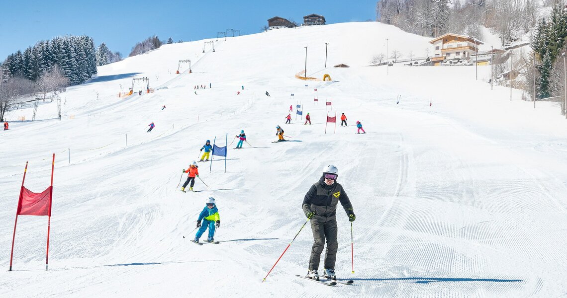 Skischüler fahren Slalom auf einer sonnigen, präparierten Piste. | © TVB Piesendorf Niedernsill - Harry Liebmann