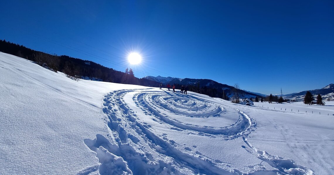 Footprints forming a spiral in the snow on a sunny winter landscape with mountains in the background.