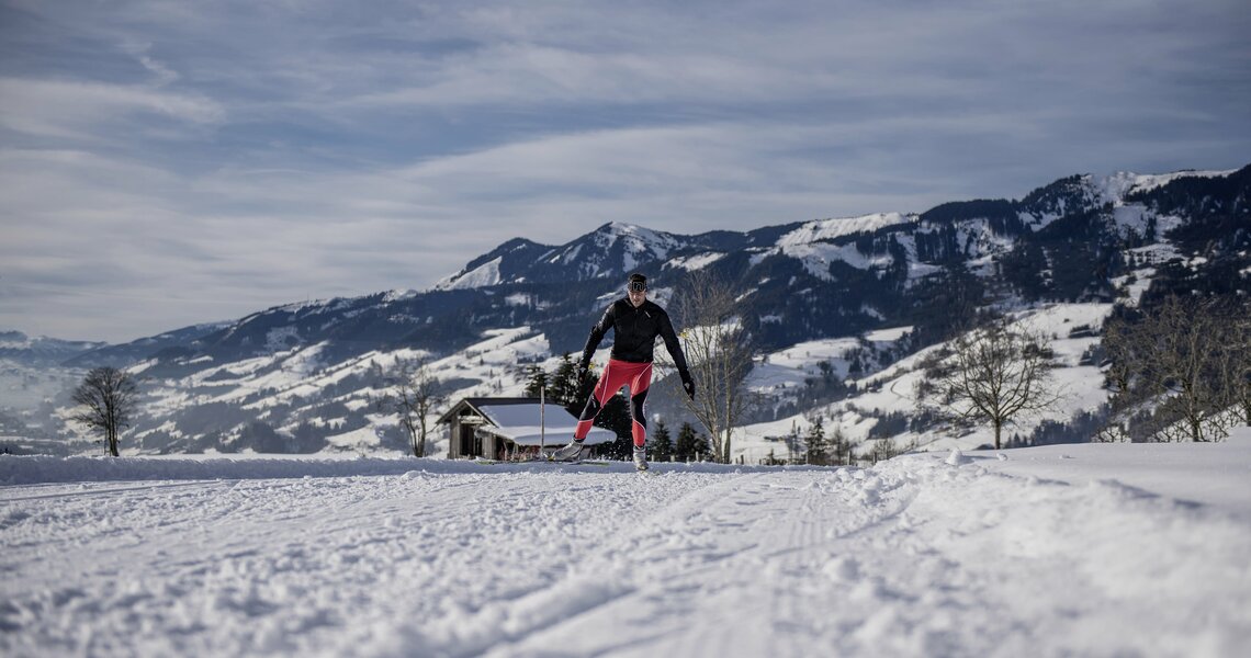 Langläufer auf gespurter Loipe vor verschneiter Berglandschaft bei Sonnenschein. | © Embach-Lend