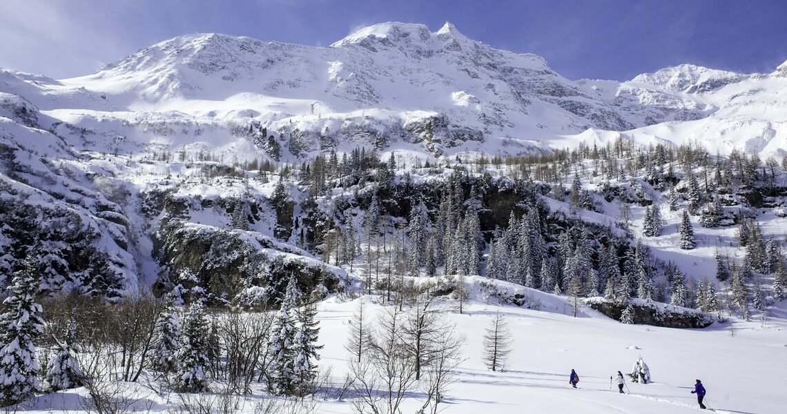 Ski tourers hiking through a snowy landscape with mountains in the background. | © Florian Bachmeier