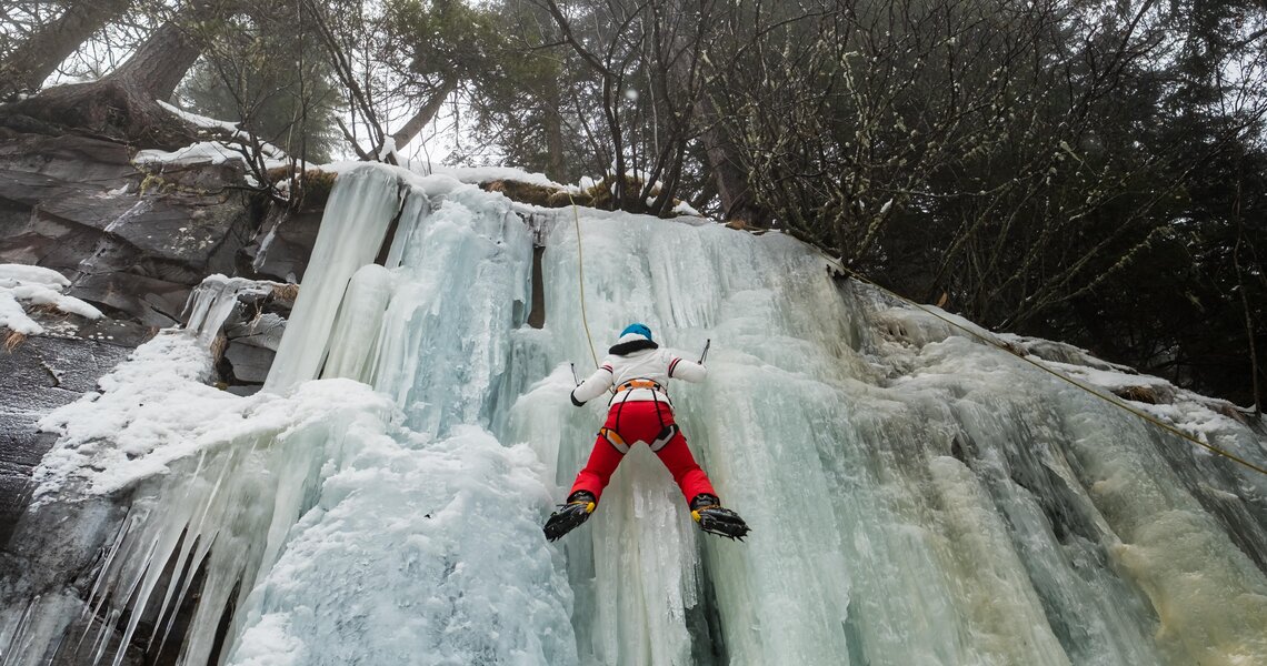 Person beim Eisklettern an einer gefrorenen Wasserfallwand im Wald. | © David Innerhofer