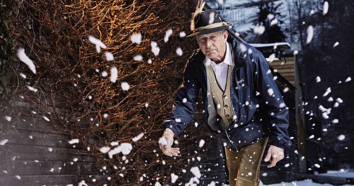 Elderly man playing ice stock sport in snowfall at dusk. | © Michael Hochfeller