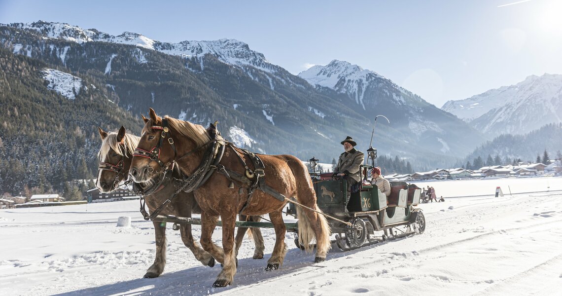 Pferdekutsche im Schnee vor Alpenkulisse bei Sonnenschein.