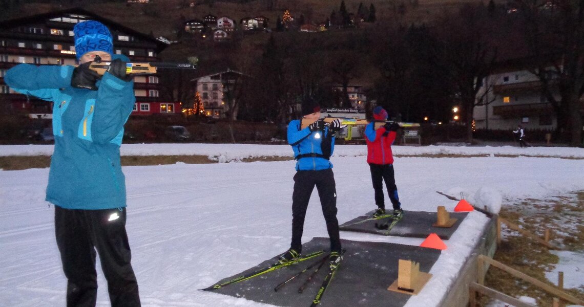 Three people training for the biathlon on cross-country skis in a wintry setting.
