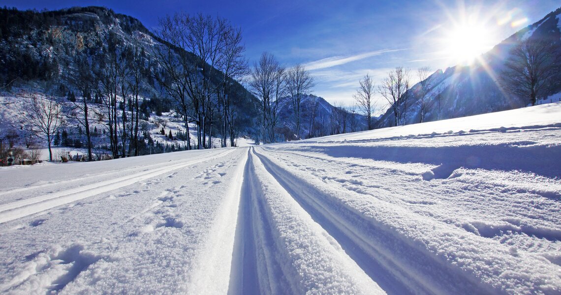 Langlaufloipe im Sonnenschein mit verschneiter Winterlandschaft im Tal.